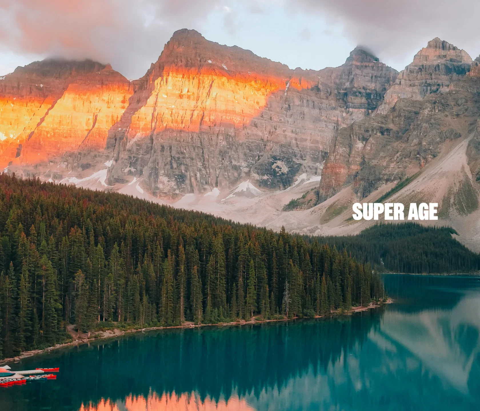 Mountain landscape at sunset with pine forest and lake in foreground; text "SUPER AGE" appears on the right over the trees.