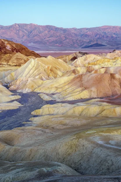 Eroded, multicolored badlands and hills under a clear sky, with distant mountains in the background.